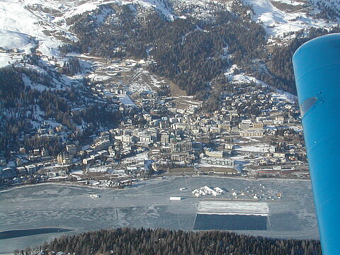 Zugefrohrener See mit der Stadt St. Moritz.